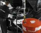Mechanik wymienia olej w czarnym BMW. Duży, pomarańczowy bęben z napisem "Motul" sugeruje, że to czas na regularną wymianę oleju.