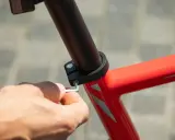 Dłoń dokręca śrubę imbusową mocującą sztycę w ramie czerwonego roweru.