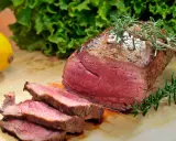 Saftiges Roastbeef mit perfekter kerntemperatur medium, garniert mit Rosmarin. Daneben ein Zitronen- und Salatblatt.
