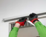 Man con guantes rojos y negros instala riel para puerta corredera.