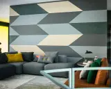 Un salon moderne avec un canapé gris et un mur orné d'un motif géométrique audacieux. Une idée motif peinture murale qui crée une illusion de profondeur.