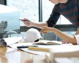 Deux architectes discutent d'un plan sur un écran, utilisant un système de gestion de contenu d'entreprise pour organiser leurs documents.
