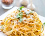 Pyszne spaghetti aglio olio, posypane parmezanem i natką pietruszki, z płatkami chili w tle.