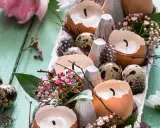 Osterdeko selber basteln mit Naturmaterialien: Eierschalenkerzen, Wachteleier und zarte Blüten auf Holz.