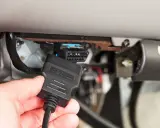 Ręka podłącza kabel OBD II do złącza diagnostycznego pojazdu, aby sprawdzić błędy DTC.