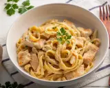 Pyszne makaron tagliatelle z kurczakiem w kremowym sosie, udekorowane natką pietruszki. Idealne danie na obiad.