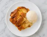 Un délicieux pain perdu au four, doré et moelleux, servi avec une boule de glace à la vanille sur une assiette blanche.