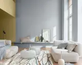 Sala de estar con paredes en tonos grises y mostaza, muebles claros y alfombra con diseño orgánico. Ideales colores suaves para pintar una casa.