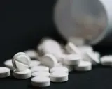 Białe tabletki, w tym jedna z nacięciem, rozsypane z białego pojemnika. Antybiotyk bez recepty.