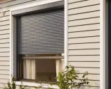 Volet roulant gris fermé sur une fenêtre de maison avec bardage beige.