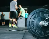 Pierwszy trening na siłowni plan. W tle ludzie ćwiczący, na pierwszym planie talerz obciążeniowy.