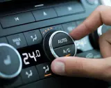 Dedo ajustando el dial del aire acondicionado del coche para comprobar el compresor. Se ve la pantalla digital con 24.0 grados.