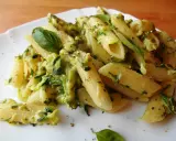 Penne z kremowym sosem i startą cukinią, ozdobione listkami bazylii. Pyszny makaron z cukinią na białym talerzu.