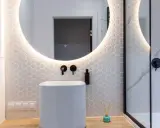 Baño moderno con lavabo blanco, espejo redondo con luz LED y azulejos hexagonales. ¿Cuánto cuesta reformar un baño así?