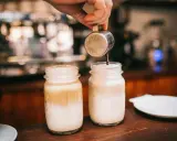 Barista bereitet Latte Macchiato zu. Die Frage "wie viel Kalorien hat ein Latte Macchiato" beschäftigt viele Genießer.