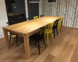 Stilleben matbord i trä med svarta och gula stolar. Bakom syns en fondvägg med trädmotiv.