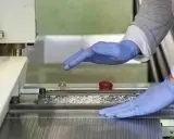 Manos enguantadas operan una máquina que parece ser una cizalla, lista para cortar material.