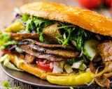 Duży kebab w bułce z mięsem, warzywami i sosem na drewnianym tle.