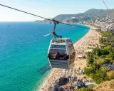 Seilbahn über dem belebten Alanya Strand mit türkisfarbenem Meer und vielen Sonnenanbetern.