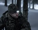 Mężczyzna w zimowej, kamuflującej kurtce i czapce z czołówką Olight, gotowy na wyprawę w góry.