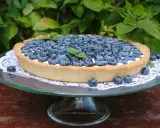 Pyszna tarta z borówkami, udekorowana listkami mięty, prezentuje się apetycznie na szklanej paterze.