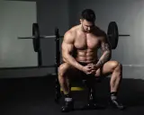 Muskulöser Mann sitzt nach dem Training auf einer Bank, bereit für die Definitionsphase seines Trainingsplans.