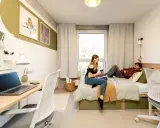 Dwoje studentów w pokoju, marzących o darmowych studiach zaocznych. Na biurku laptop, na łóżku relaks.