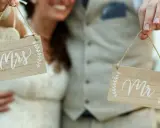 Para Młoda trzyma tabliczki "Mrs" i "Mr", symbolizujące zmianę nazwiska po ślubie.