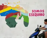 Mural przedstawiający mapę Wenezueli z flagą i hasłem "Somos Esequibo". Dwóch chłopców na skuterze przejeżdża obok.