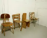 Tre unika stolar står uppradade. En av dem, med en böjd rygg, påminner om en design av Finn Ahlgren.