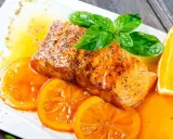 Delicioso salmón a la naranja, jugoso y dorado, servido con rodajas de naranja fresca y una salsa vibrante.