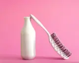Eine weiße Flasche, die wie ein **collagen shampoo** aussieht, lehnt an einer Haarbürste auf rosa Hintergrund.