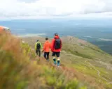 Tre vänner på vemdalen vandring njuter av den vidsträckta utsikten över skogar och berg under en molnig himmel.