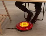 Persona calentando sus pies con un brasero eléctrico rojo bajo un escritorio.