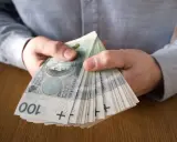 Dłonie trzymające plik banknotów 100 zł. Symbolizuje to zarobki, które mogą być wynikiem najlepiej płatnych zawodów.