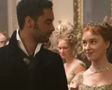 En ung kvinna med tiara och en man i elegant klädsel möts med blickar. Kanske en scen från rollistan i familjen Bridgerton.