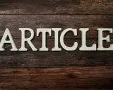 Białe litery układają się w słowo "ARTICLE" na drewnianym tle. To zapowiedź rozszerzonego artykułu po angielsku.
