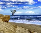Sandige Klippen am playa del cable, mit einer Plattform im Meer unter dramatischem Himmel.