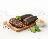 Kaszanka pokrojona na plastry, całe kawałki, musztarda, czosnek i przyprawy na desce.