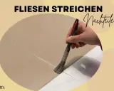 Fliesen streichen Nachteile: Eine Hand streicht mit einem Pinsel über Fliesen. Die Farbe ist hellbraun.