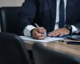 Prawnik w garniturze pisze piórem na dokumencie przy biurku.