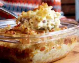 En sked lyfter upp en portion krämig, gammaldags makaronipudding ur en glasform.