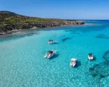 Traumhafter zypern strand mit kristallklarem Wasser und vier Booten, die vor der felsigen Küste ankern.