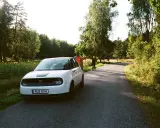 Vit elbil parkerad vid en skogsväg, två personer står vid sidan. En perfekt start på en roadtrip Sverige.