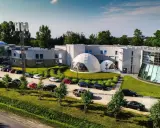 Nowoczesne polskie hotele niezależne z kopułami i przeszklonymi fasadami, otoczone zielenią i parkingiem pełnym samochodów.