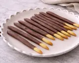 Assiette de mikado maison, bâtonnets de biscuit enrobés de chocolat, avec quelques grains de café à côté.