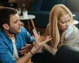 Hombre con expresión de enfado gesticula hacia su pareja, quien lo mira con desprecio, evidenciando una discusión.