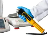 Ręka w rękawiczce trzyma alco sensor 4. Obok wagi laboratoryjne.