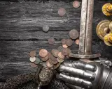 Schwert, Münzen, Ritterhandschuh und Kerzenleuchter auf dunklem Holz. Die Münzen könnten die Vasallen Bedeutung symbolisieren, die für ihren Lehnsherrn kämpften und bezahlten.