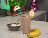 Ein leckerer schoko protein shake mit Banane und einem lustigen Regenbogen-Strohhalm. Daneben eine Schale mit Quark.
